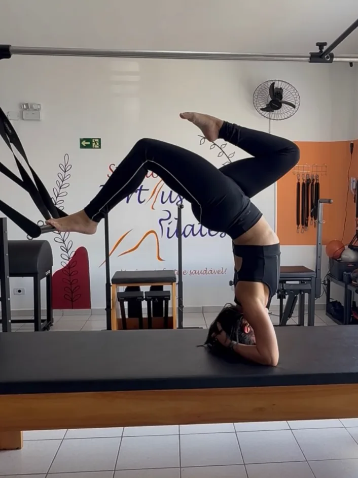 Aluna em posição invertida sobre o aparelho de pilates, no Studio Fortius, com a parede laranja ao fundo